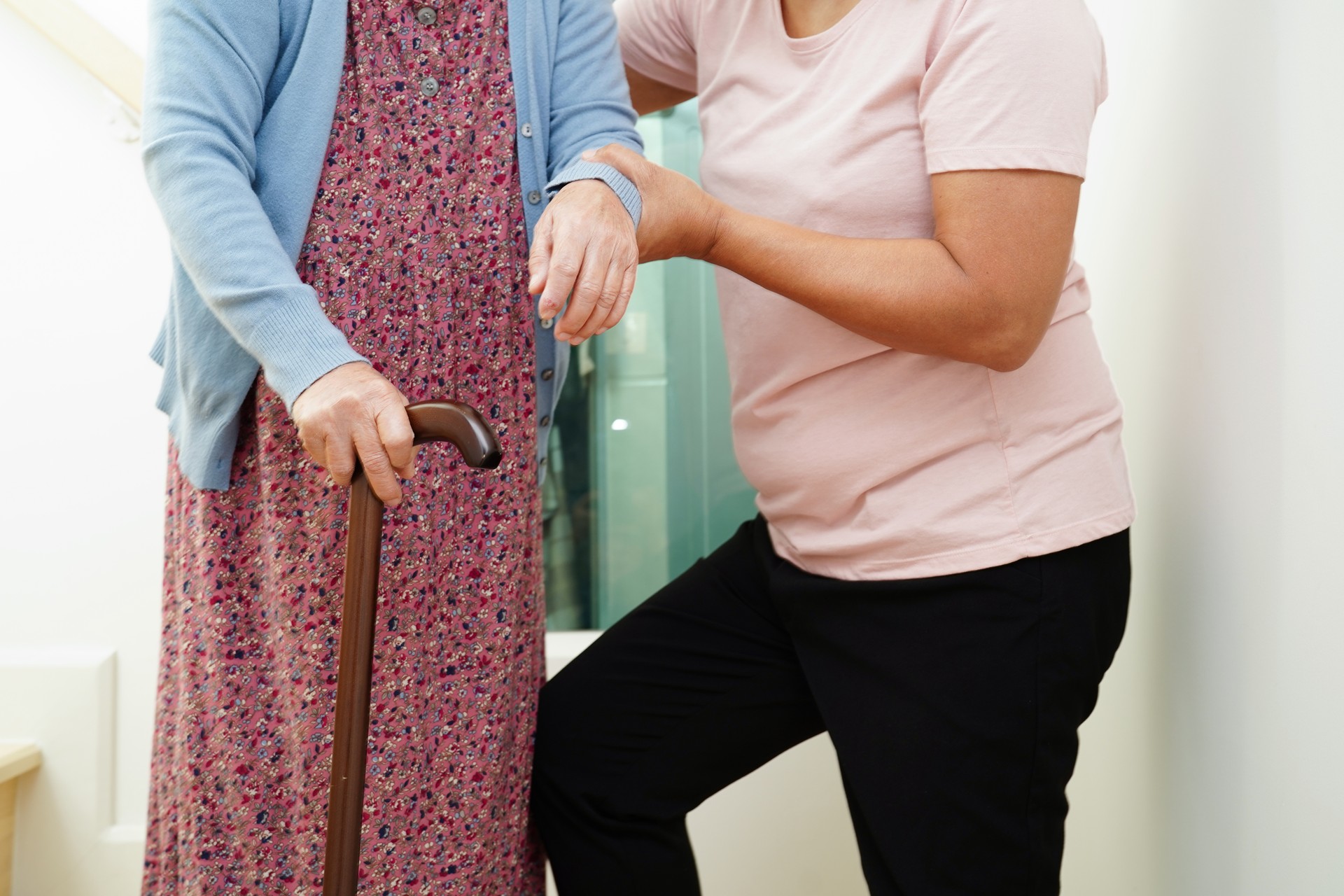 Asian senior woman use walking stick with caregiver help support walking down the stairs prevent accident, slip and fall at home.